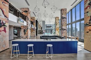 Eine geräumige Lobby mit einer zentralen Bar, hohen Decken und großen Fenstern mit Blick auf die Stadt.