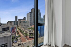 A view from a hotel room with a large window overlooking a cityscape with high-rise buildings and palm trees. - X Lounge IX Signature | 3 BR/3 Ensuite Residence (Miami)