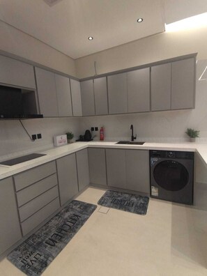 Une cuisine moderne avec des meubles gris, un lave-vaisselle noir et un plan de travail blanc.