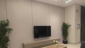 A modern living room with a flat-screen TV, a wooden coffee table, grey sofas, and potted plants. - OrbitNet - A05 (Madina)