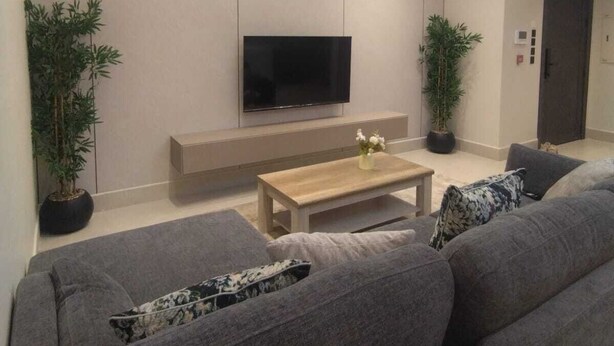 A modern living room with a flat-screen TV, grey sofas, a wooden coffee table, and two potted plants. - OrbitNet - A05 (Madina)
