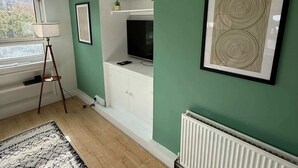 A living room with a television on a white cabinet, a floor lamp, and a framed abstract artwork on the wall.