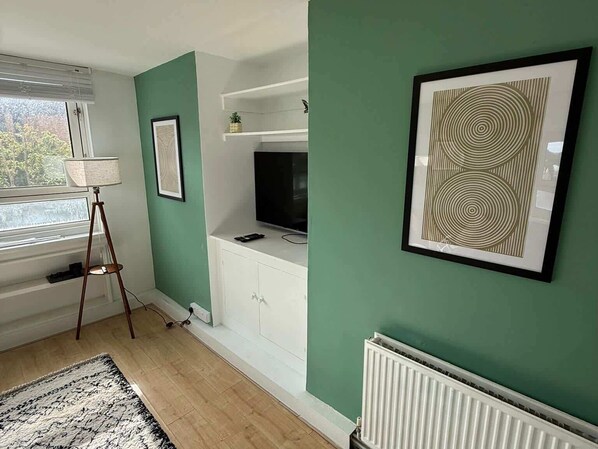 A living room with a television on a white cabinet, a floor lamp, and a framed abstract artwork on the wall.