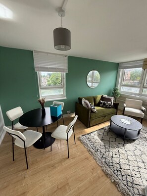 Een kamer met een eettafel, stoelen, een bank, een ronde salontafel en een spiegel aan de muur.