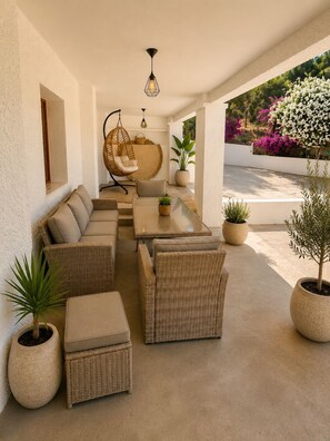 Un espacio al aire libre con mobiliario de mimbre, una silla colgante y plantas en macetas.