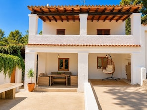 A two-story building with a balcony, a hanging chair, and a table with cushions.
