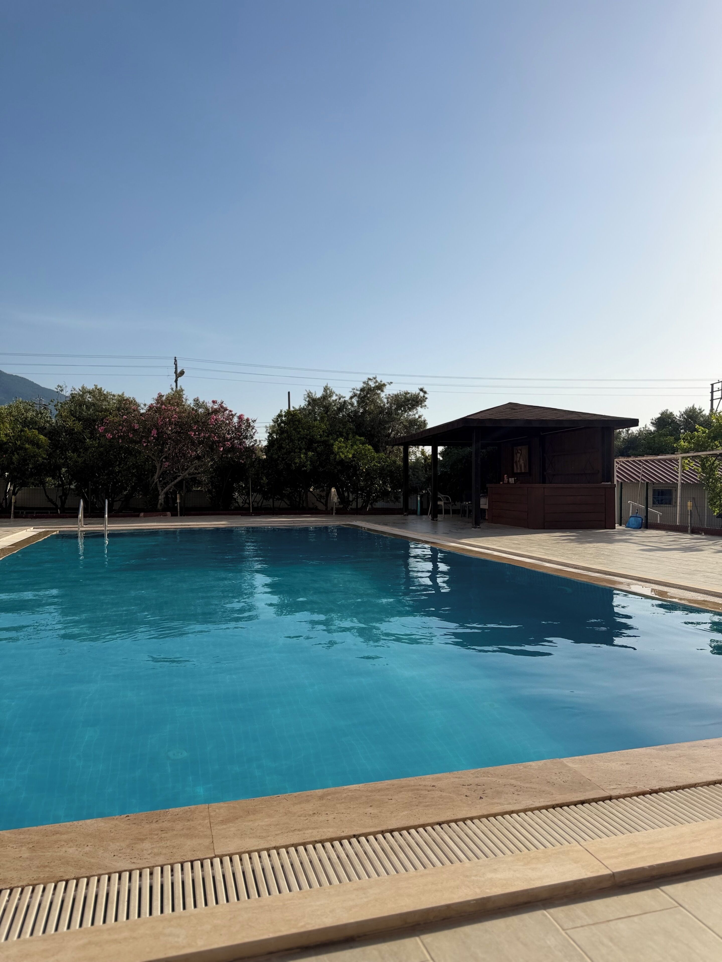 Una piscina azul cristalina con una terraza de madera y un edificio pequeño al fondo.