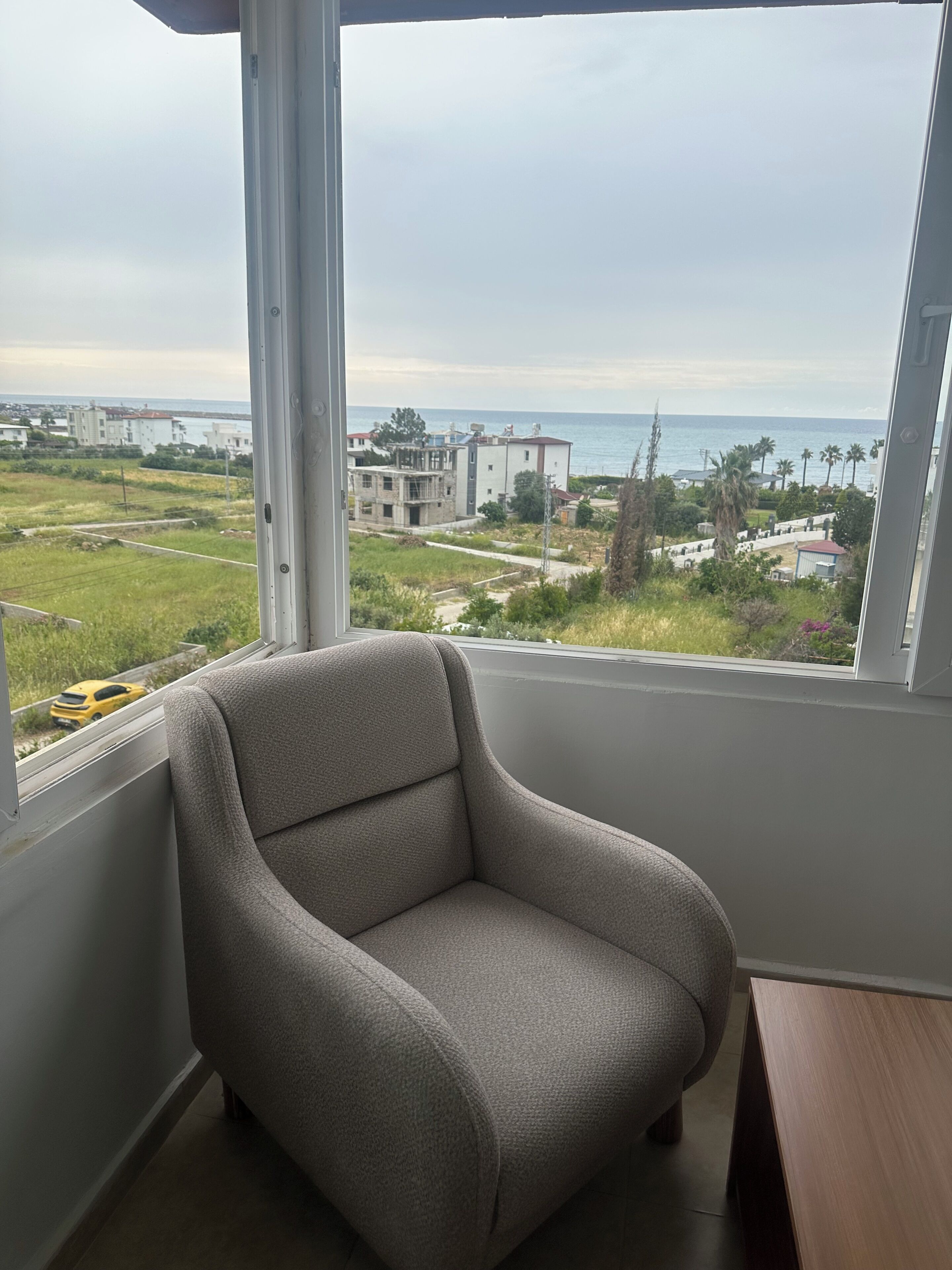 Um quarto com uma janela grande, uma poltrona cinza e uma mesa de madeira.