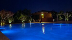 A swimming pool at night with a covered area and trees in the background. - Vera Luz Arsuz (Arsuz)