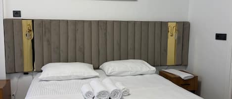 A hotel room with a large bed, two pillows, a headboard, a nightstand, a bedside table, and two framed zebra pictures on the wall.
