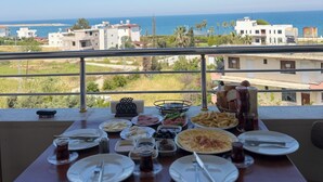 A dining table with plates, cutlery, and condiments, overlooking a coastal view with buildings and greenery. - Vera Luz Arsuz (Arsuz)