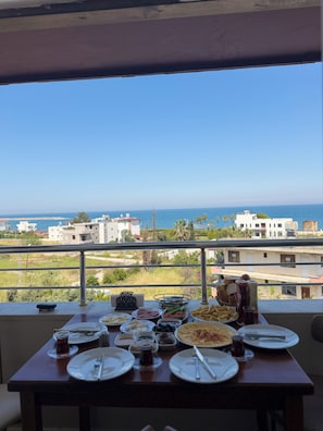 A dining table with plates, cutlery, and condiments, overlooking a coastal view with buildings and greenery. - Vera Luz Arsuz (Arsuz)