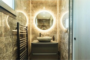 Un baño con pared de mármol, un espejo redondo, un lavabo tipo cuenco y un perchero para toallas.