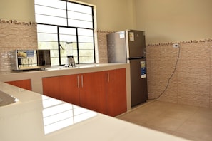 A kitchen with a refrigerator, microwave, and a window with blinds.