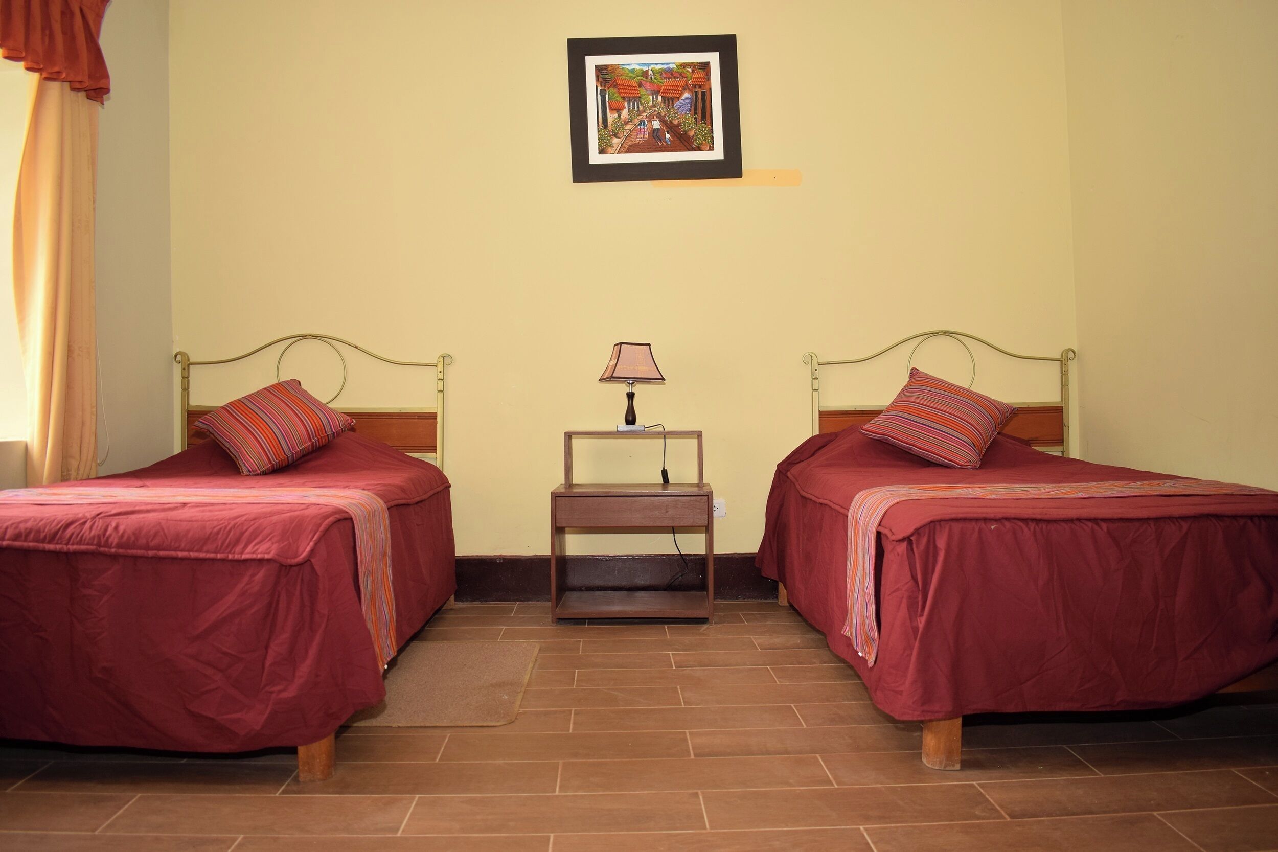 A room with two beds, a nightstand with a lamp, and a framed picture on the wall.