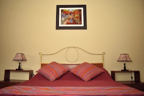 A bed with a red bedspread, two striped pillows, a headboard, and a framed picture on the wall.