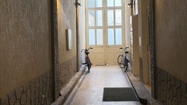 Ein Korridor mit Fliesenboden, einer Tür am Ende und Fahrrädern, die an der Wand lehnen.