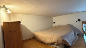 Eine kleine Einzimmerwohnung mit einem Holzschrank, einem Bett mit Matratze und Kissen sowie einer Deckenleuchte.