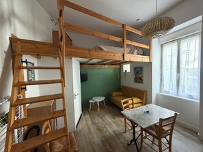 Ein Loft-Zimmer mit Holzleiter, Etagenbetten, einem Esstisch und einer Wand in Grüntönen.