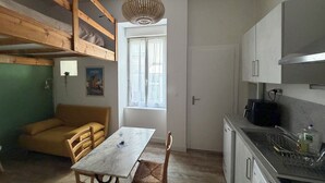 Eine kleine Küche mit Esstisch, fest eingebautem Backofen und einem Fenster mit Vorhängen.