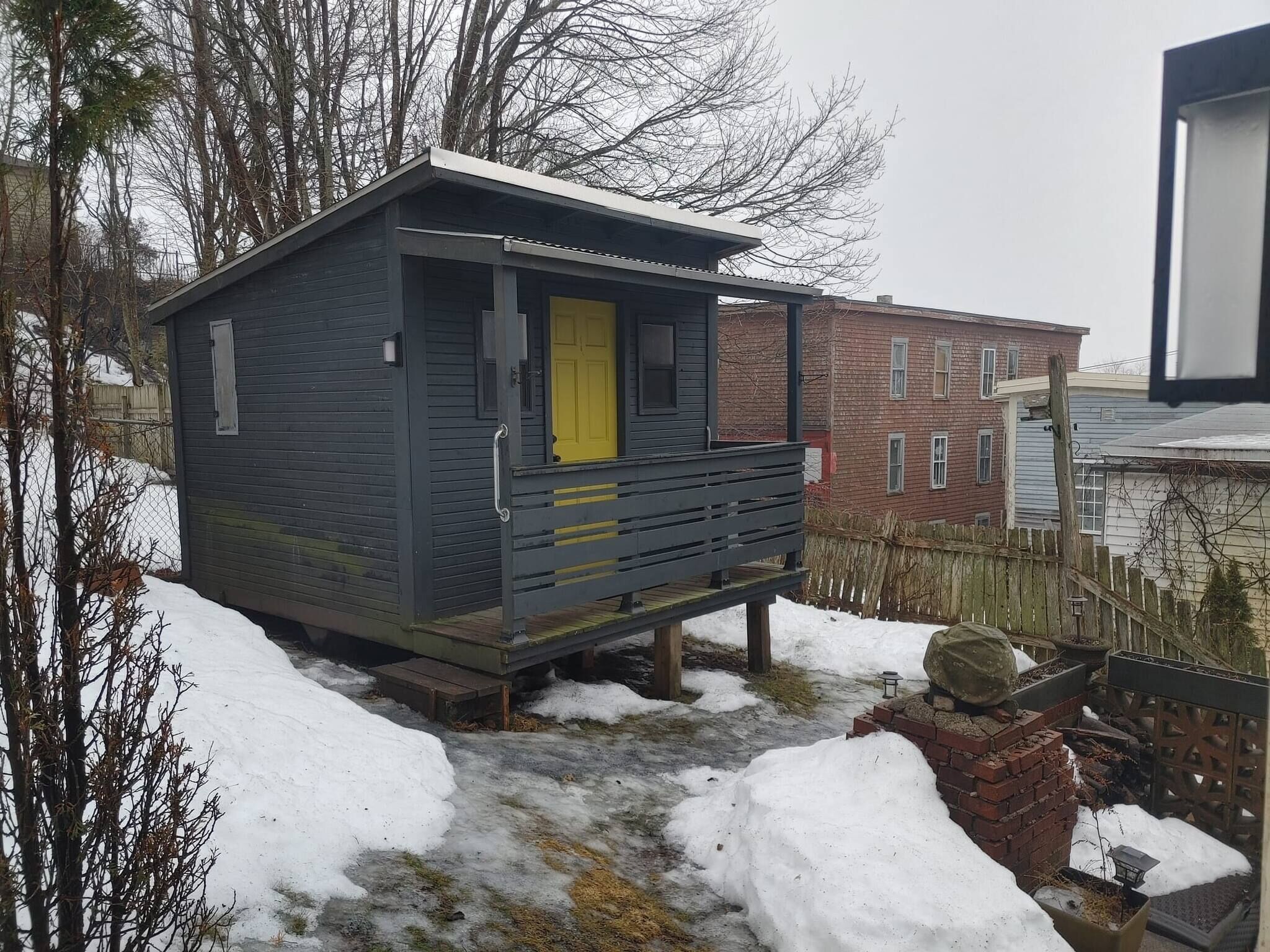 A small, dark-colored cabin with a yellow door, a porch, and a brick base.