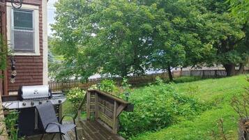 A backyard with a barbecue grill, a wooden deck, and a wooden fence.