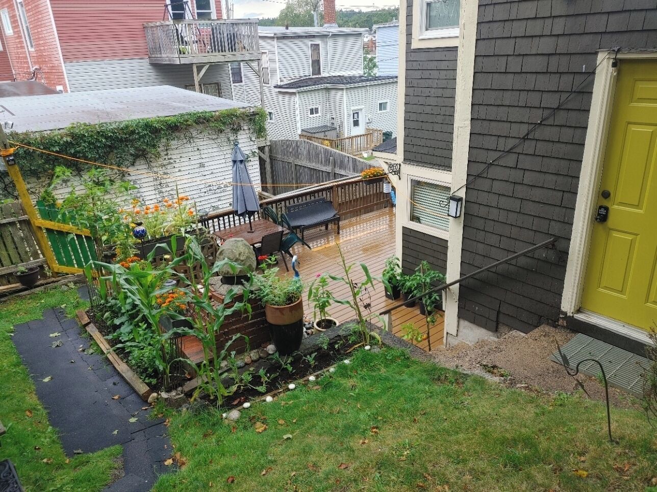 Un patio trasero residencial con una terraza de madera, jardineras y una puerta amarilla.