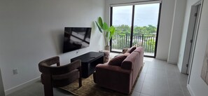 Ein Wohnzimmer mit Fernseher, Sofa, Sessel und einem großen Fenster mit Blick.