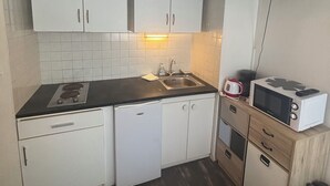 A compact kitchen with white cabinets, a black countertop, a built-in microwave, a sink, and a flat-screen TV mounted on the wall.