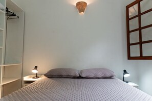 A bedroom with a bed, two bedside lamps, a wall-mounted light fixture, and a window with a wooden frame. - House with Barbecue Area and Air Conditioning in Engenho D’Água (Ilhabela)