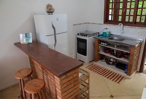 Eine kleine Küche mit Kühlschrank, Herd, Spüle und Barhocker.