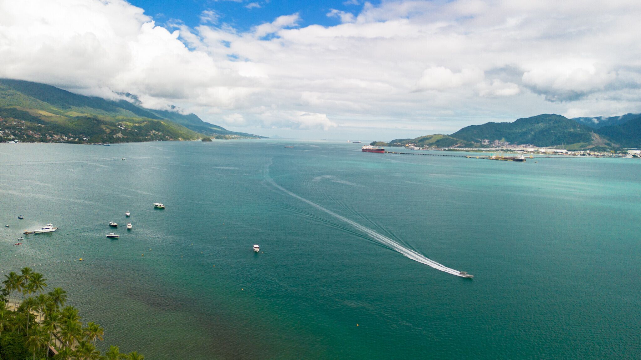 Uma região costeira com barcos, céu claro e montanhas ao longe.
