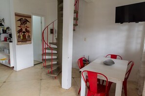 A dining area with a white table and red chairs, a staircase with red railings, and a wall-mounted TV. - House with Barbecue Area and Air Conditioning in Engenho D’Água (Ilhabela)
