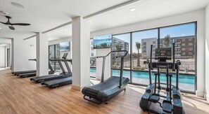 Ein Fitnessraum mit Laufbändern, einem Rudergerät und Blick auf einen Pool.