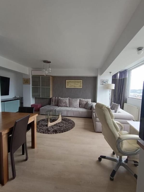 A modern hotel room with a dining table, sofa, and a TV.