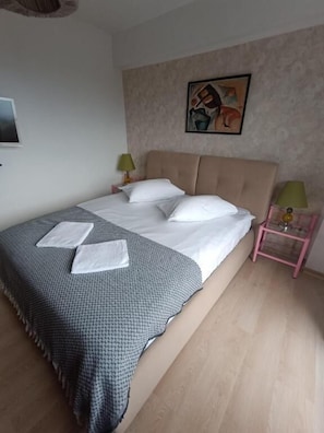 A neatly made bed with a patterned blanket, a headboard, a bedside table with a lamp, and a framed picture on the wall. - Apartament vedere panoramica Aria (Cluj-Napoca)