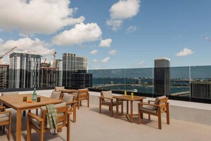 Una terraza en la azotea con mobiliario de madera, vista del horizonte urbano y grúas de construcción al fondo.
