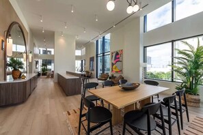Una cocina moderna con una isla central, un comedor con mesa de madera y sillas negras, y ventanas amplias con vistas a la ciudad.