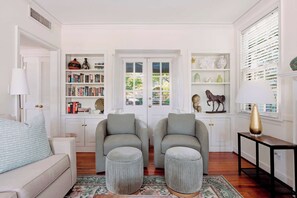 Ein Wohnzimmer mit zwei Sesseln, einem Sofa, einem kleinen Tisch und einem Bücherregal.