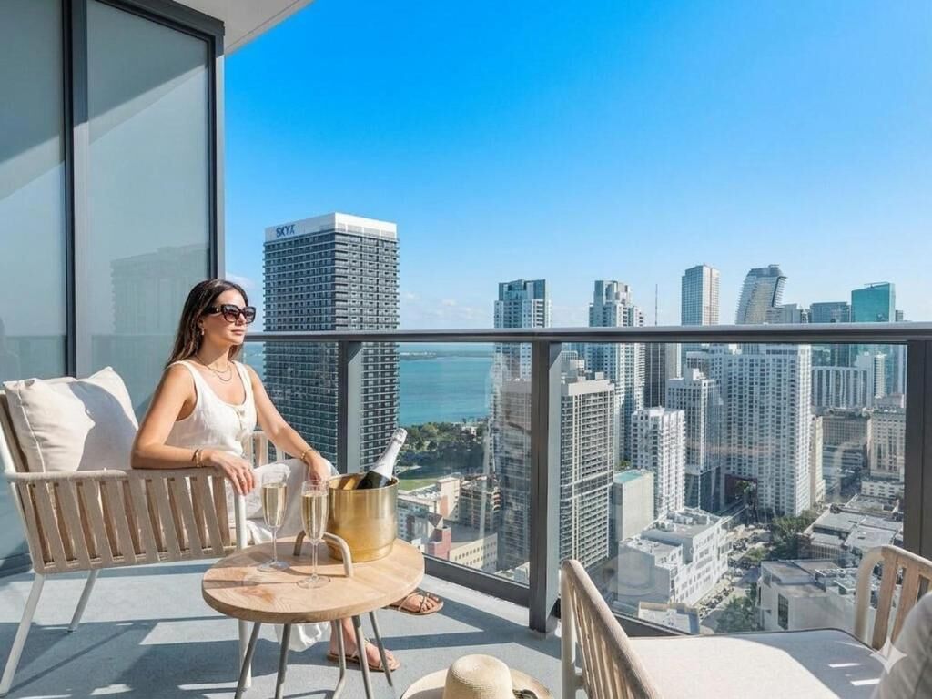 A balcony with a city view, a chair, a table with a champagne bucket, and a bottle.