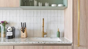 Una cocina con mostrador, pileta, cafetera, bloque de cuchillos y grifo color dorado.