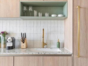 Una cocina con mostrador, pileta, cafetera, bloque de cuchillos y grifo color dorado.