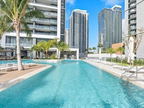 A swimming pool with lounge chairs, palm trees, and high-rise buildings in the background. - Natiivo Miami Vacation Rentals (Miami)