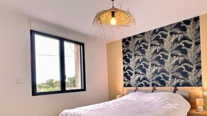 Un dormitorio con una cama, mesitas de noche, una ventana y un papel tapiz con motivos de hojas.