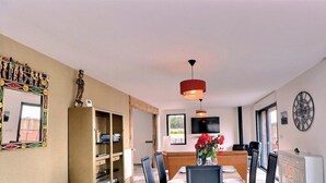 Un comedor con una mesa, sillas, un televisor montado en la pared y un ventanal con vistas al exterior.