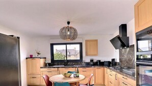 Cocina moderna con armarios de madera, un refrigerador negro, una mesa de comedor con sillas y una lámpara colgante.