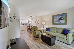 Ein modernes Wohnzimmer mit einem grünen Sofa, einem Couchtisch und einem Essbereich inklusive Tisch und Stühlen.