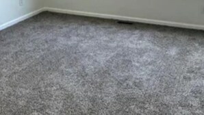 Een kamer met een groot raam, vloerbedekking en witte wanden.