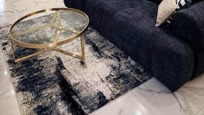 Een moderne woonkamer met een donkerblauwe bank, een ronde glazen salontafel en abstracte wanddecoratie.