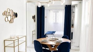 Een eetruimte met een ronde tafel, blauwe stoelen, een kroonluchter met gouden lijst en een vloer van wit marmer.